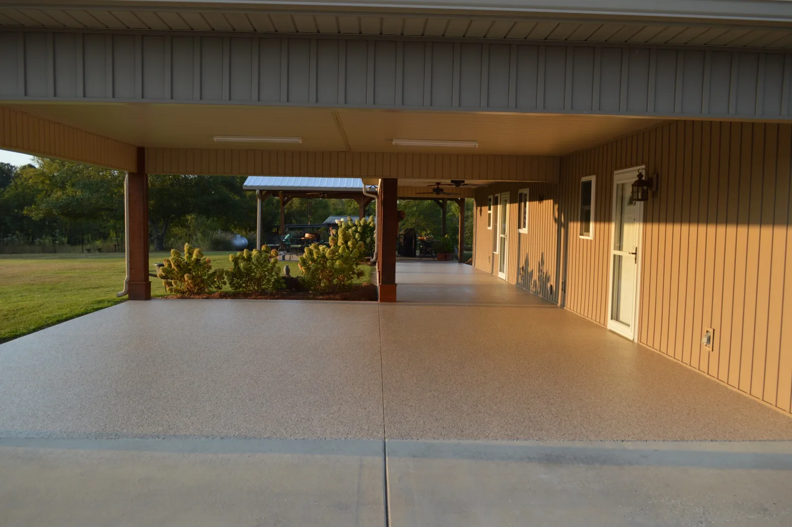 Covered carport with a tan flake floor alongside a cream clapboard house