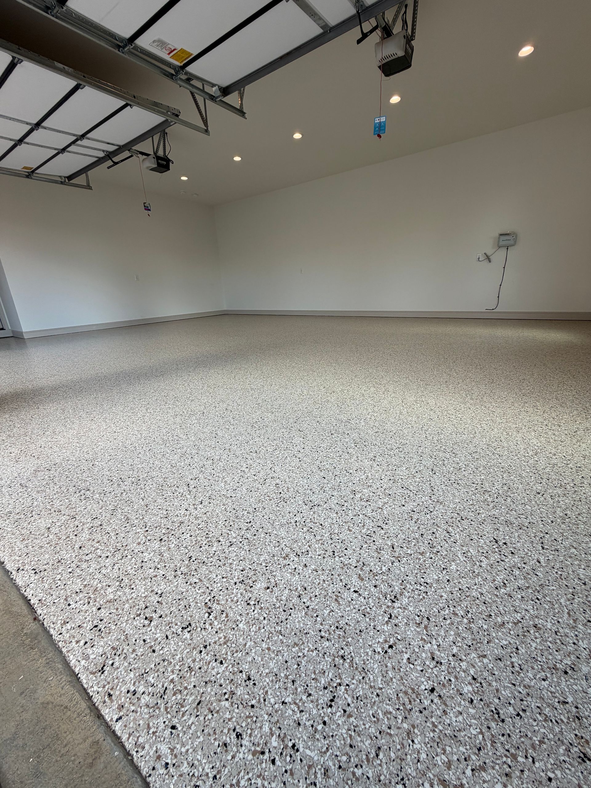 Tan and black flake floor in a two-car garage with the door open to daylight