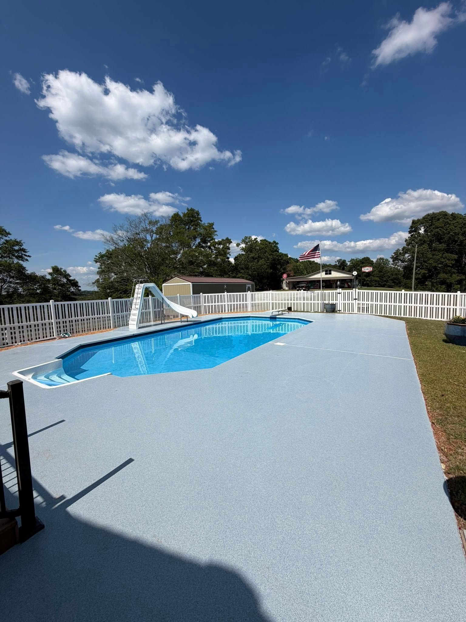 Textured pale blue pool deck coating wrapping an in-ground pool under a clear sky