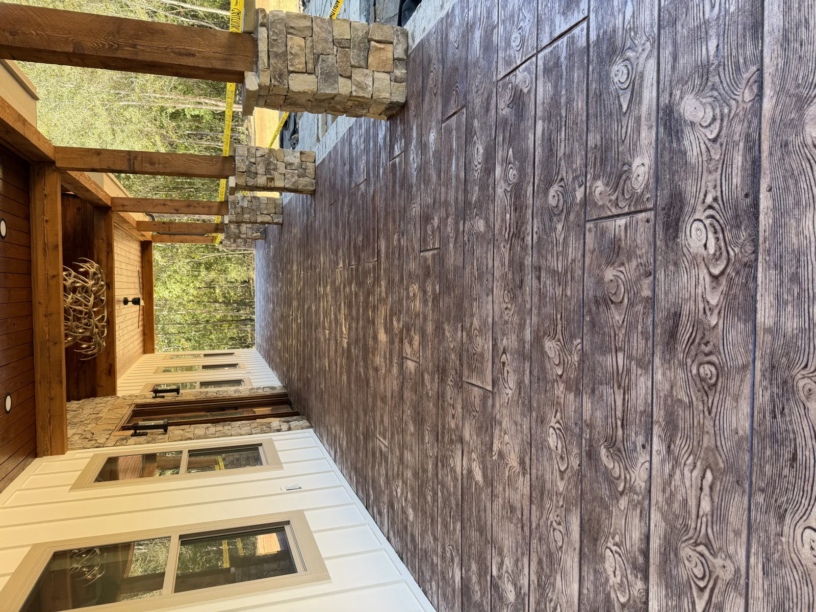 Tan flake porch with a dark border inset, wrapped by a stone wall and timber posts