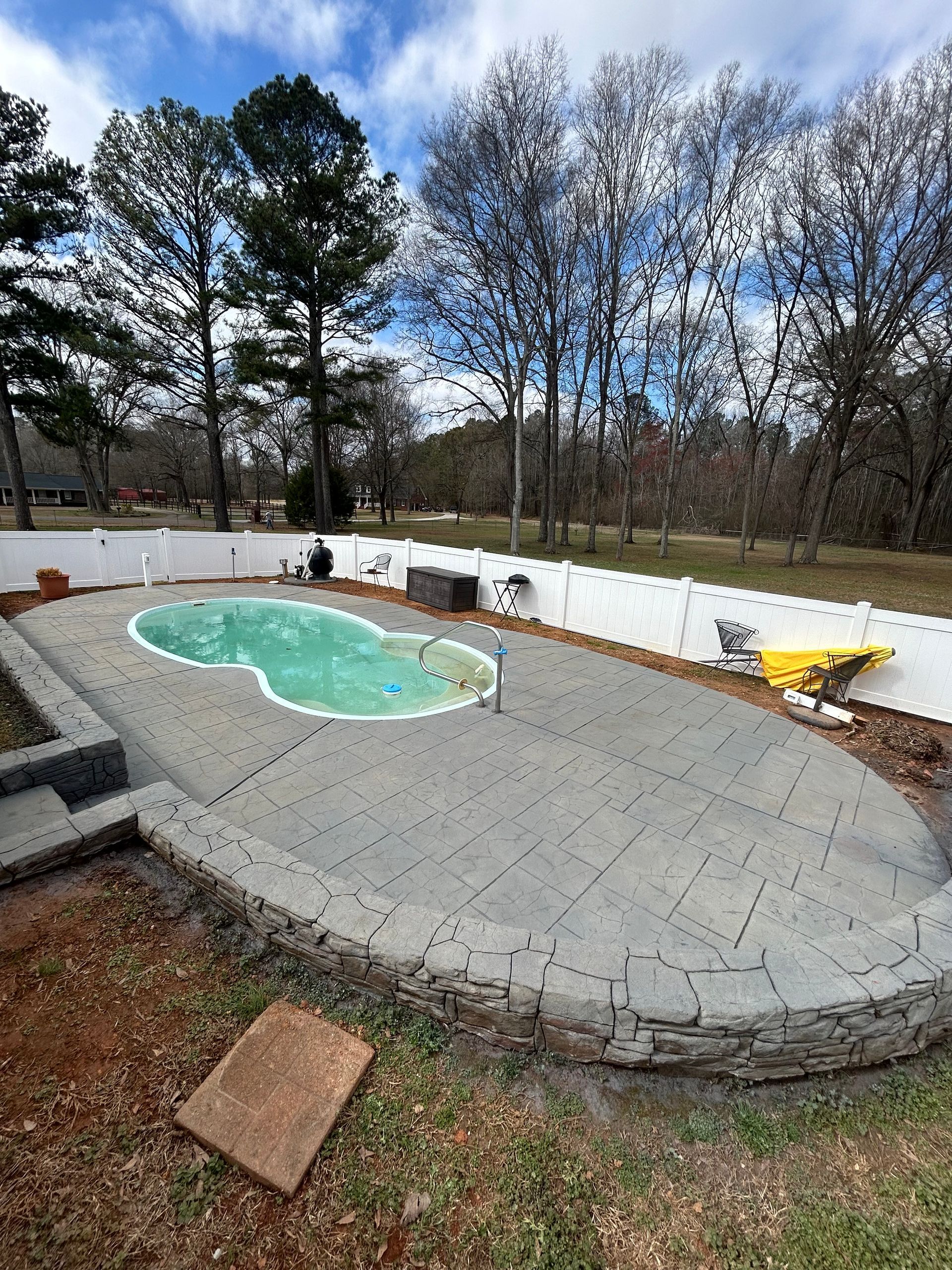 Sealed gray stamped concrete pool deck curving around a small backyard pool
