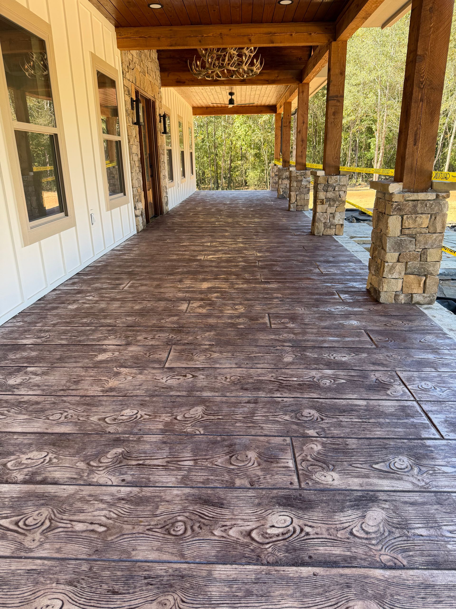 Wood-plank stamped concrete porch stained brown, running past stone columns